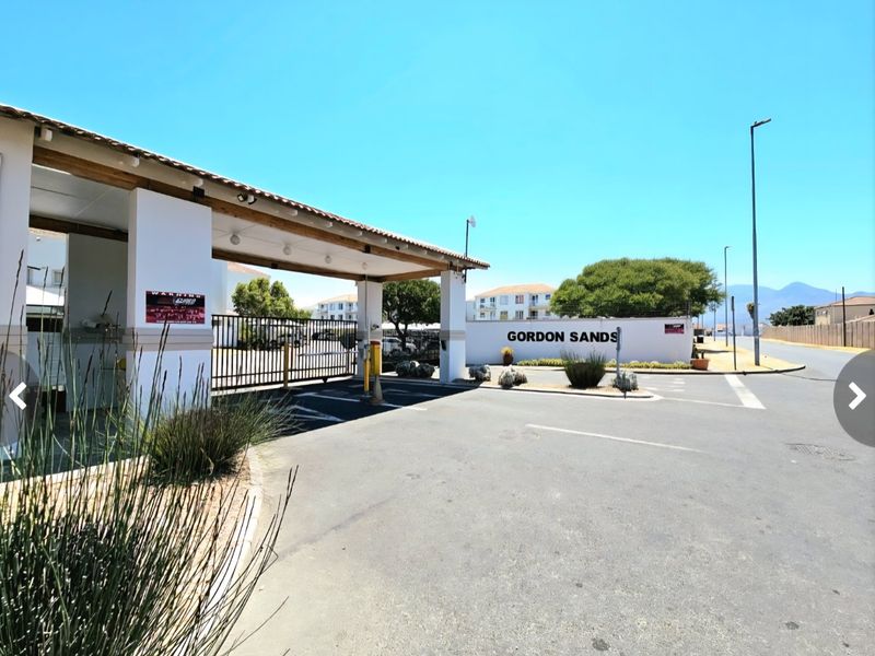 The entrance to Gordon Sands apartment complex featuring a secure gated access point, gatehouse structure, and paved driveway.