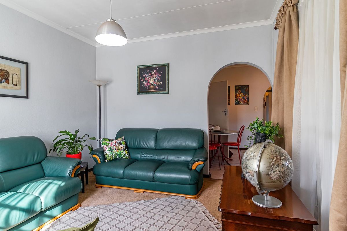 A comfortable living room featuring carpeted flooring, a coved ceiling, and an arched doorway leading to an adjacent dining area.