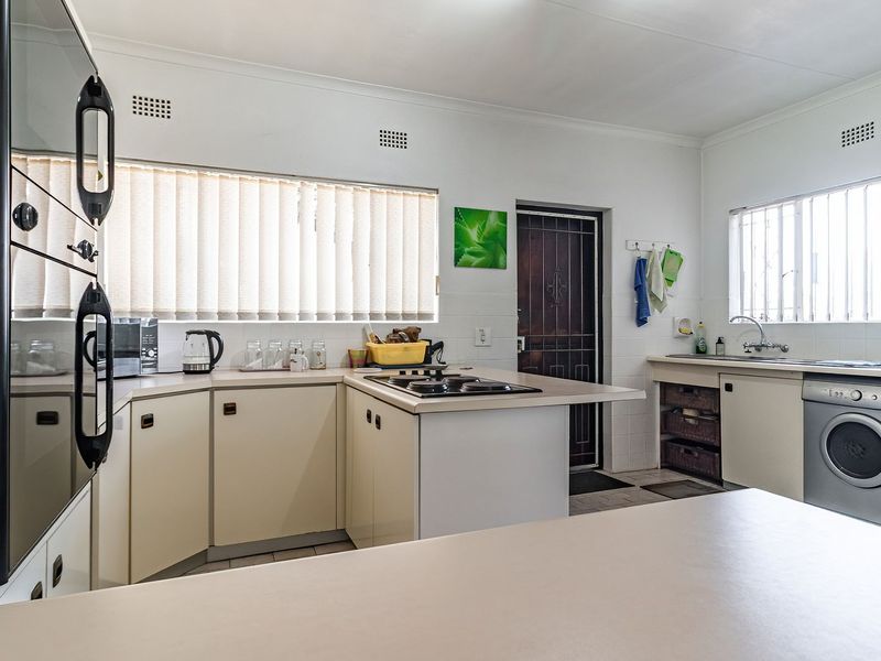 Functional kitchen featuring built-in oven, hob, double sink, and ample cabinetry with integrated laundry appliance space.