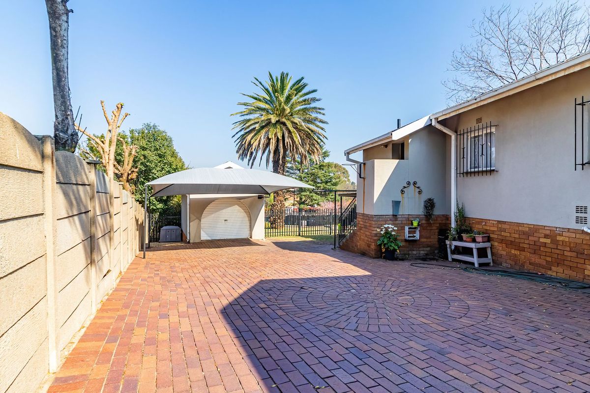 A spacious rear exterior area featuring a brick-paved driveway, a carport, and a secure garage entrance with perimeter walling.