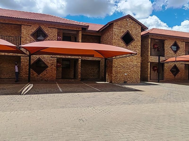 Exterior view of a face-brick apartment complex featuring paved parking areas with shade-cloth carports and distinctive diamond-shaped windows.