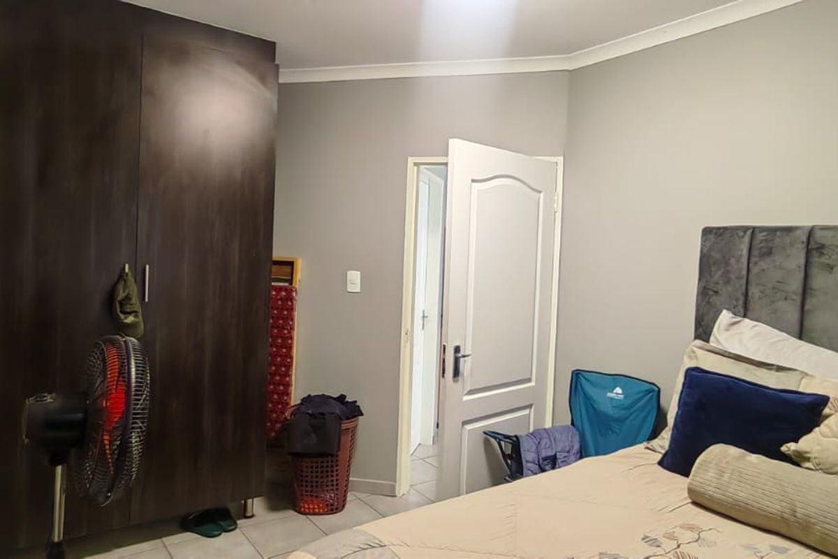 A bedroom featuring tiled flooring, a built-in dark wood wardrobe, and neutral wall finishes.