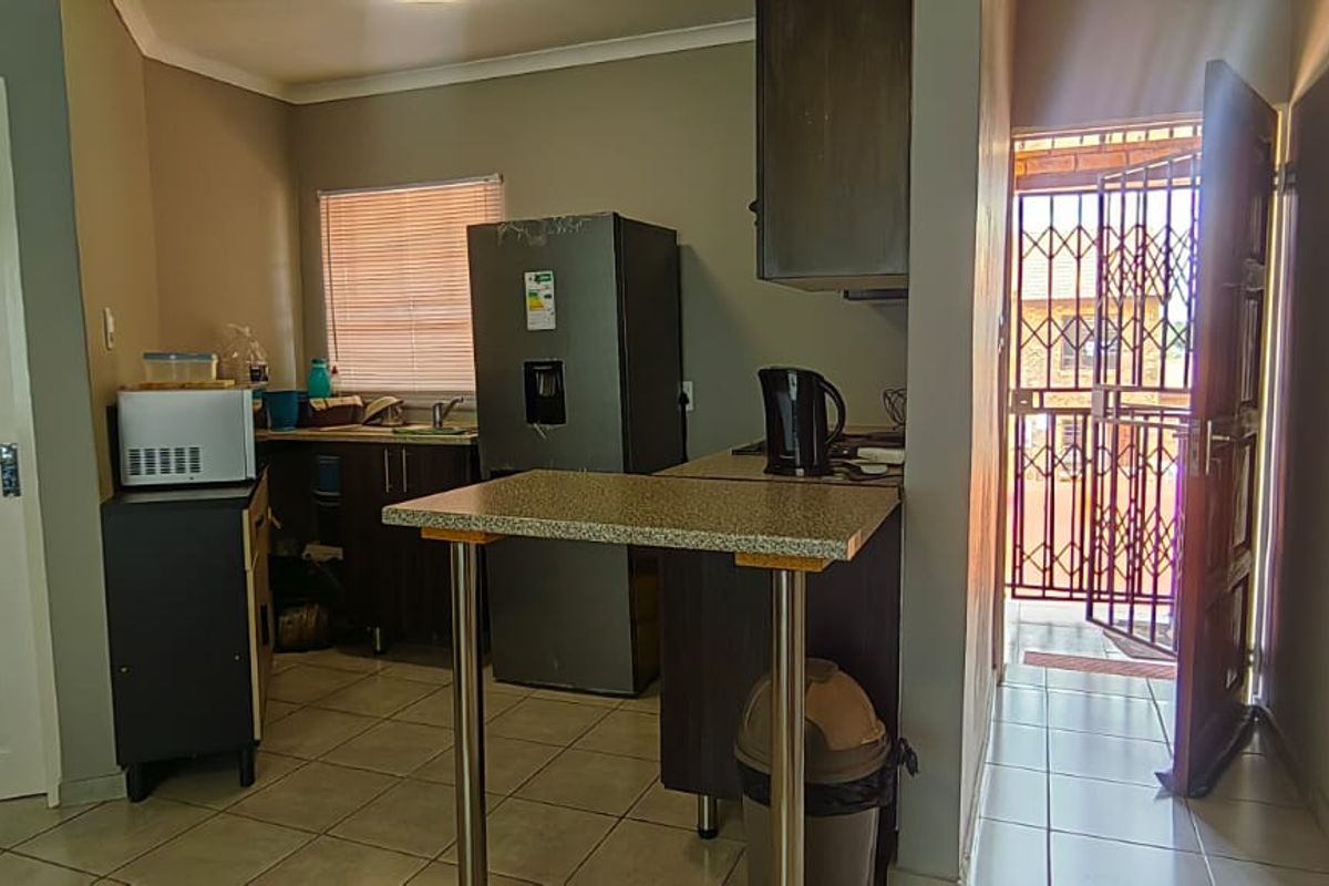 Compact kitchen area featuring built-in cabinetry, a breakfast bar, and tiled flooring, with direct access to an exterior security gate.