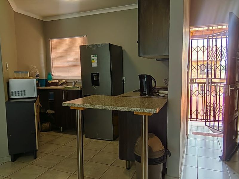 Compact kitchen area featuring built-in cabinetry, a breakfast bar, and tiled flooring, with direct access to an exterior security gate.