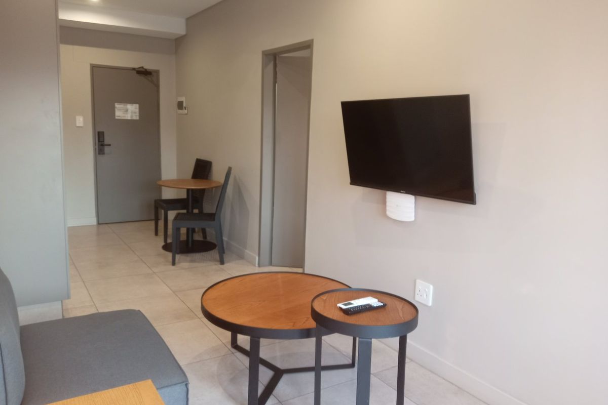 A modern living area featuring neutral wall tones, tiled flooring, and a wall-mounted television, providing a clean and functional space.