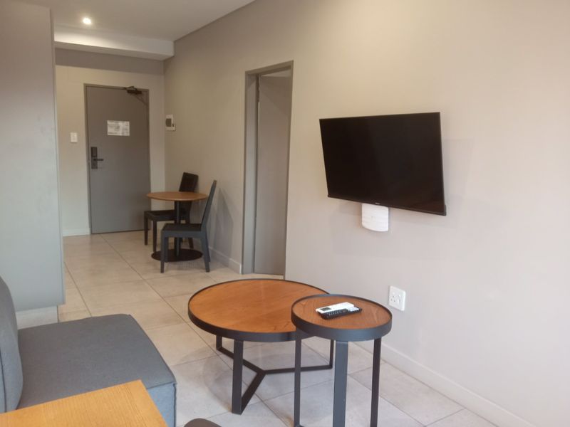 A modern living area featuring neutral wall tones, tiled flooring, and a wall-mounted television, providing a clean and functional space.