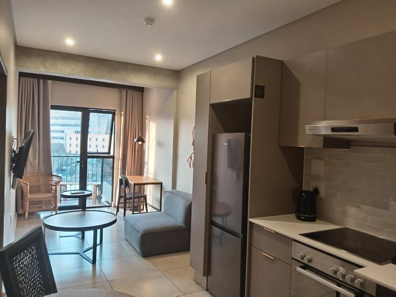 Modern open-plan apartment featuring a sleek kitchen with built-in appliances, tiled flooring, and direct access to a private balcony.