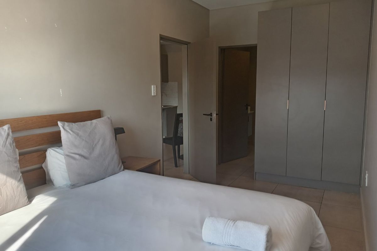 A functional bedroom featuring neutral wall tones, tiled flooring, and a built-in wardrobe, with direct access to adjacent rooms.
