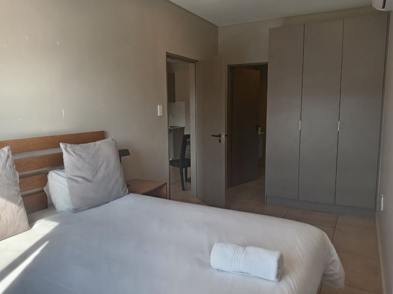 A functional bedroom featuring neutral wall tones, tiled flooring, and a built-in wardrobe, with direct access to adjacent rooms.