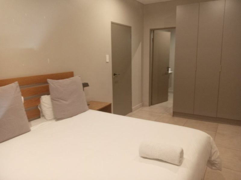 A modern bedroom featuring neutral tones, tiled flooring, and ample built-in cupboard storage with direct access to an adjoining room.