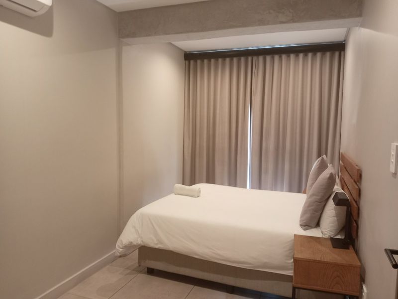 A well-maintained bedroom featuring tiled flooring, an air conditioning unit, and an exposed concrete beam detail, finished with neutral wall tones.