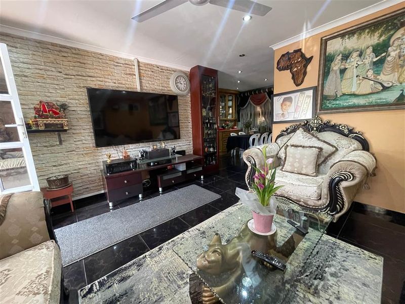 A living room featuring a textured stone accent wall, dark tiled flooring, and recessed lighting, with an open-plan layout leading to the dining area.