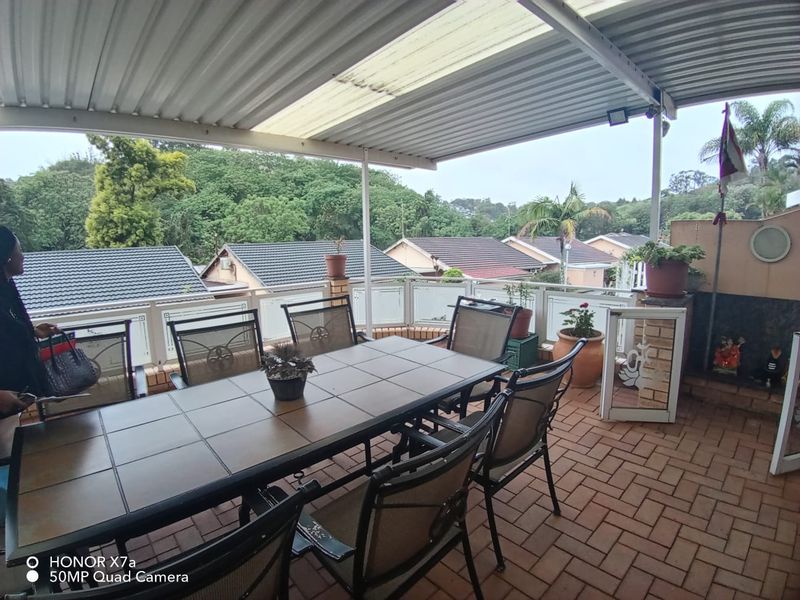 Covered outdoor patio featuring brick paving, a protective roof structure, and glass balustrades with views of the surrounding neighborhood.