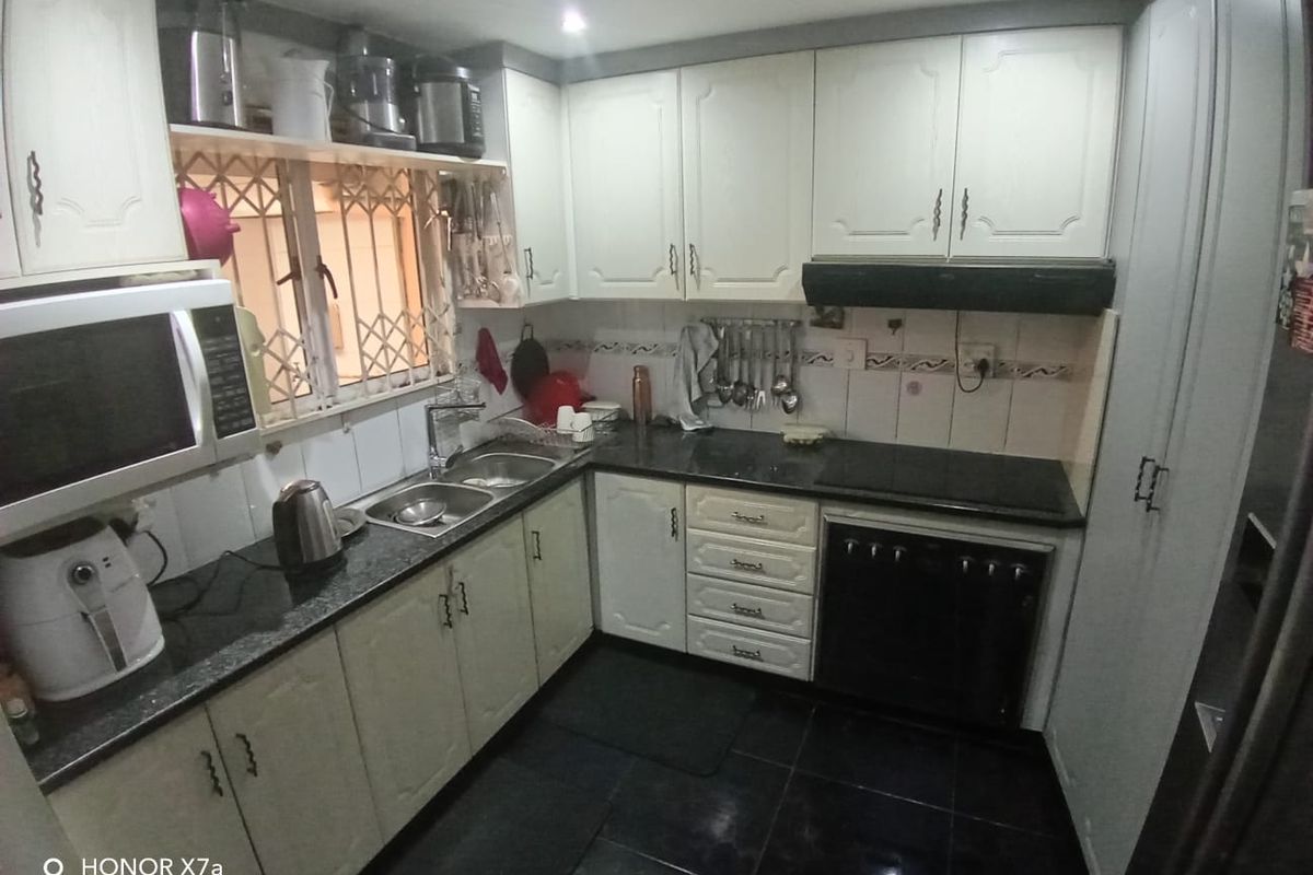 A functional kitchen featuring white cabinetry, black granite countertops, built-in oven and hob, and a double basin sink with a security-gated window.
