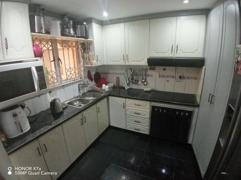 A functional kitchen featuring white cabinetry, black granite countertops, built-in oven and hob, and a double basin sink with a security-gated window.
