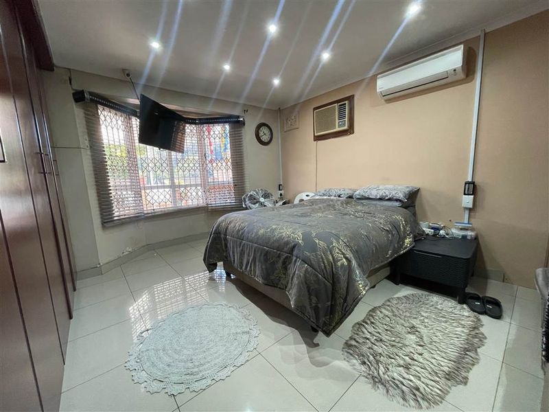 Bedroom featuring tiled flooring, built-in cupboards, recessed downlighting, and a wall-mounted air conditioning unit.