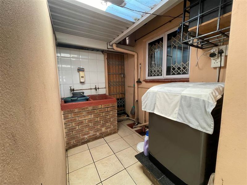 A functional outdoor laundry area featuring a brick-built sink, tiled flooring, and a covered roof structure with security features.