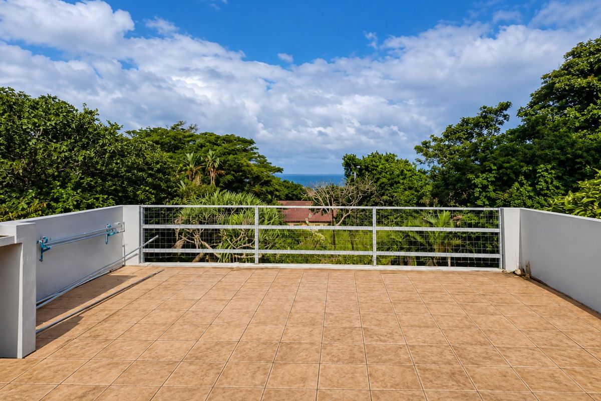 An open-air balcony featuring tiled flooring, a secure metal wire mesh railing, and a wall-mounted drying rack, offering pleasant outdoor space.