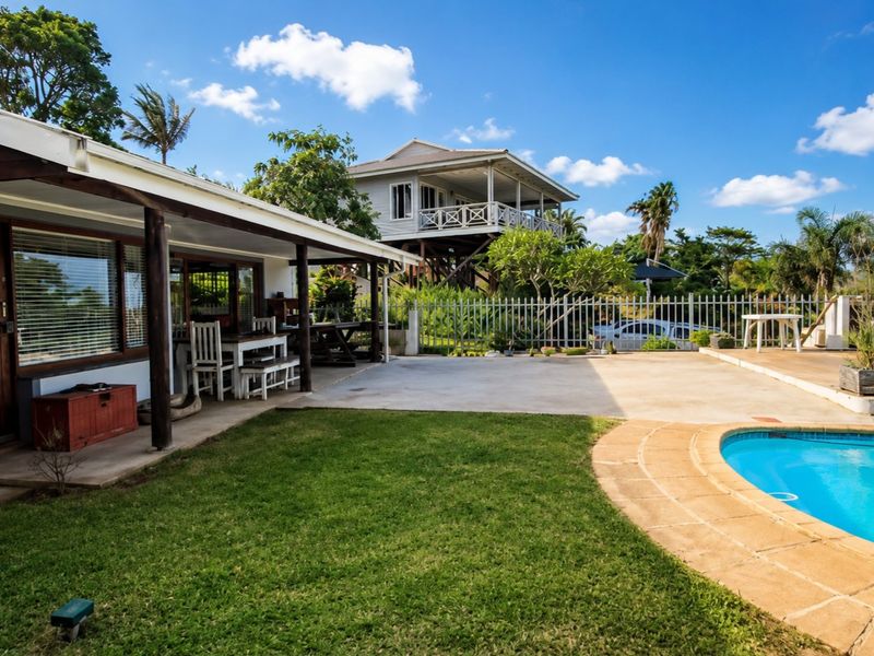 Outdoor entertainment area featuring a swimming pool, concrete patio, and covered veranda, set within a landscaped garden with perimeter security fencing.