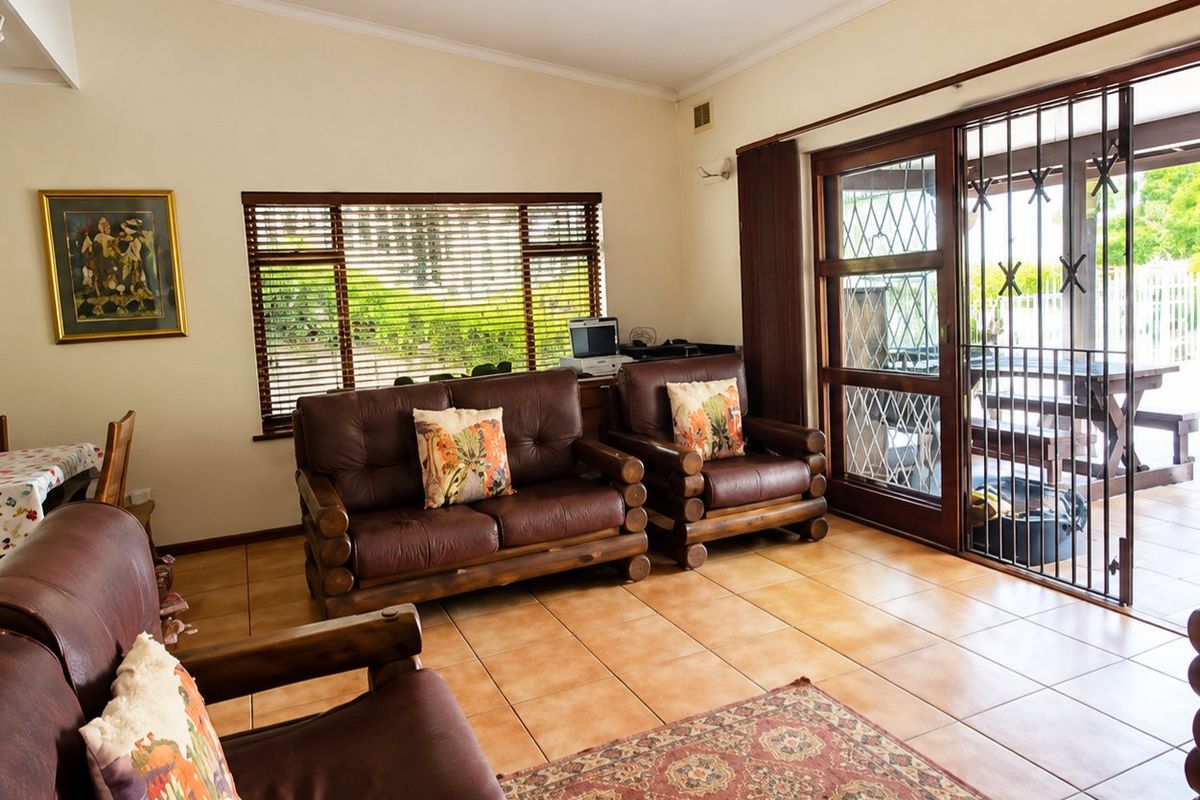 A living room featuring ceramic tile flooring, large windows with venetian blinds, and a sliding glass door leading to an outdoor patio area.