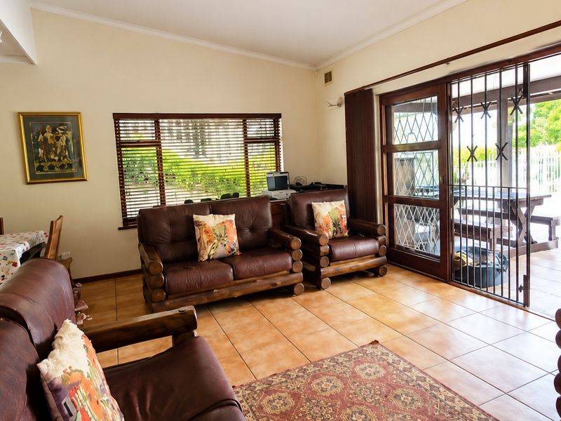 A living room featuring ceramic tile flooring, large windows with venetian blinds, and a sliding glass door leading to an outdoor patio area.