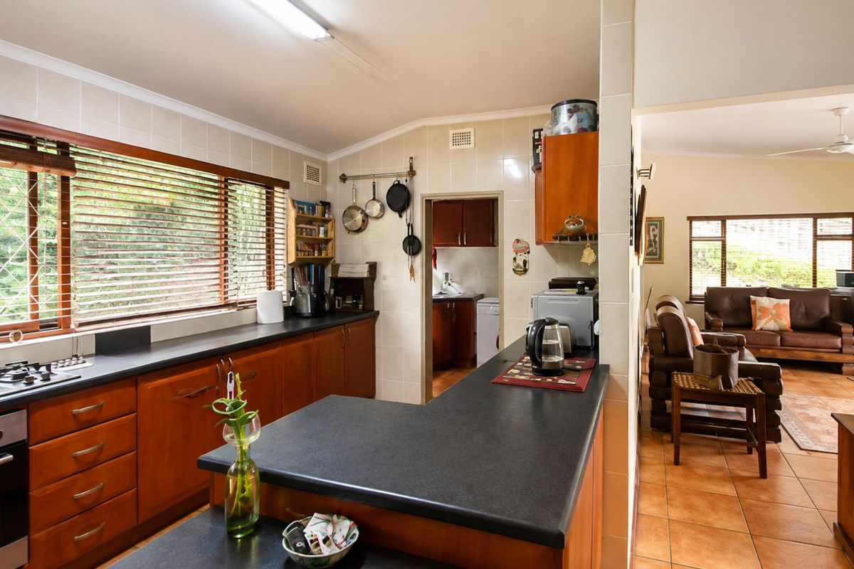 Open-plan kitchen featuring wooden cabinetry, dark countertops, and a gas hob, flowing into an adjacent living area with tiled flooring throughout.