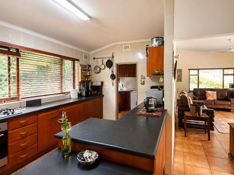 Open-plan kitchen featuring wooden cabinetry, dark countertops, and a gas hob, flowing into an adjacent living area with tiled flooring throughout.