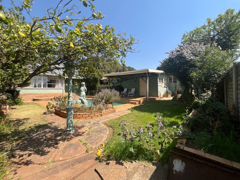 A private backyard featuring a swimming pool, brick-paved patio area, covered outdoor space, and established garden landscaping.