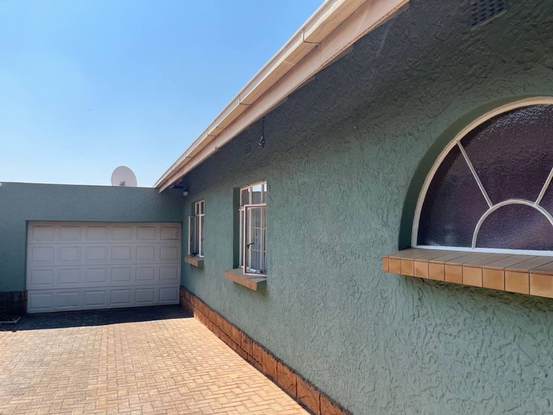 Side view of the property featuring a paved driveway, garage access, and a distinctive arched window with tiled sill.