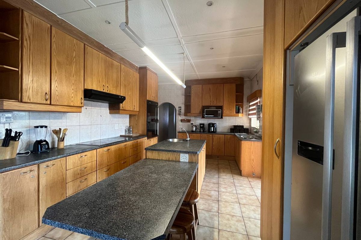 Spacious kitchen featuring extensive wooden cabinetry, a central island with breakfast bar, tiled flooring, and integrated appliances.