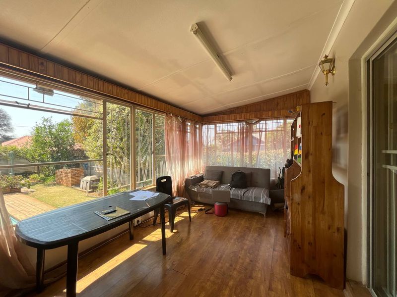 A sunroom or enclosed patio featuring large windows, wood-look flooring, and timber wall paneling, offering a bright space with views of the garden.