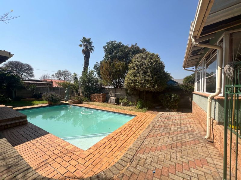 Outdoor pool area featuring a swimming pool surrounded by brick paving and established garden boundaries.