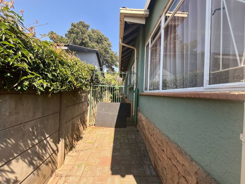 A side passage of the house featuring paved flooring, a precast boundary wall, and a metal security gate.