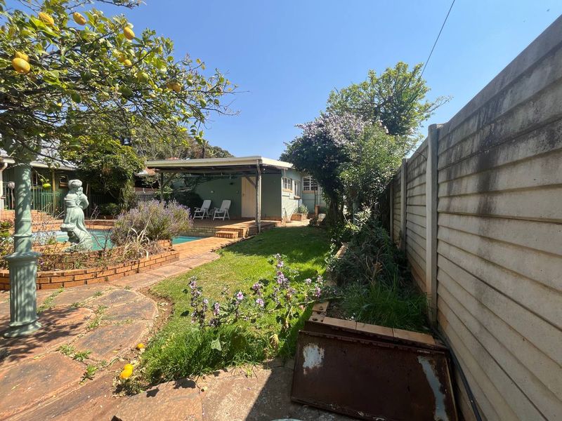 Rear garden area featuring a swimming pool, covered patio, and established landscaping enclosed by a precast concrete boundary wall.