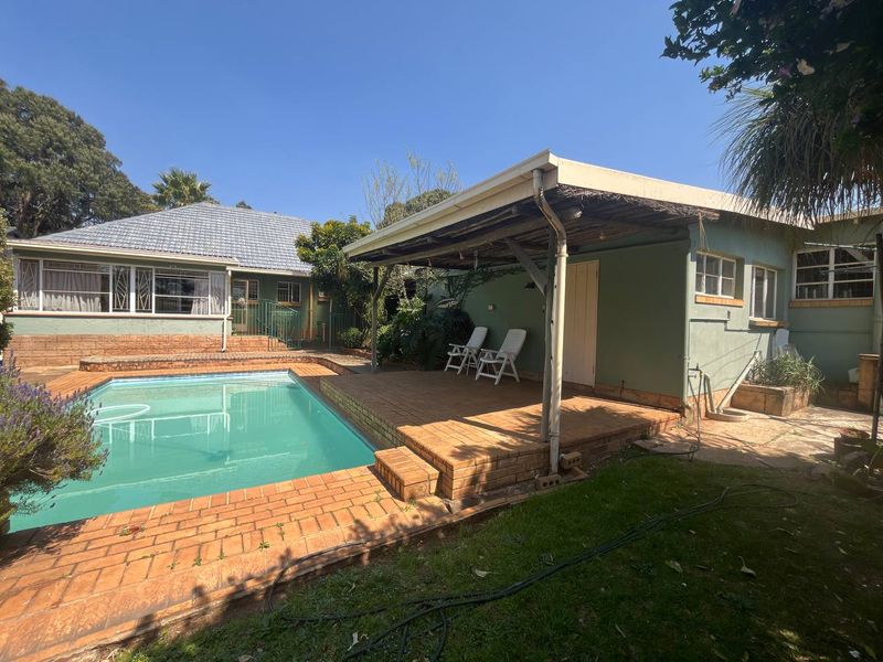Outdoor entertainment area featuring a swimming pool and a covered brick-paved patio with a thatched roof structure.
