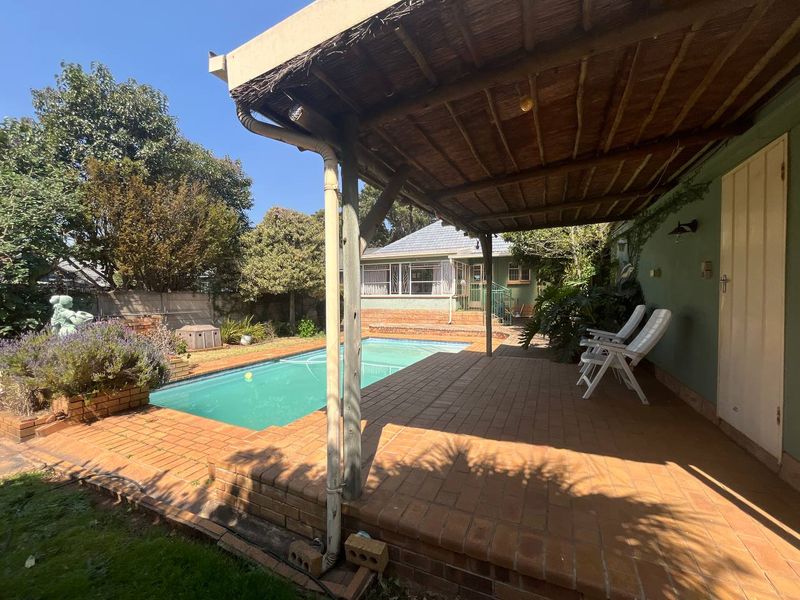 Outdoor entertainment area featuring a swimming pool and a covered patio with a thatched roof, set within a private garden.