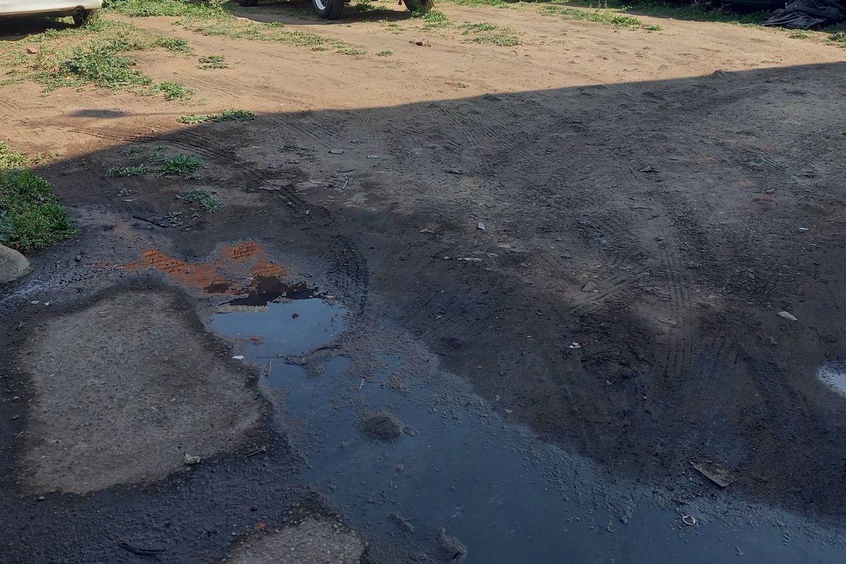 An unpaved, uneven residential land plot showing signs of poor drainage and standing water.