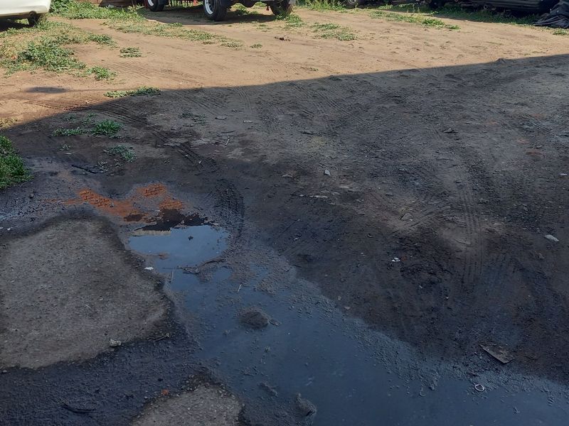 An unpaved, uneven residential land plot showing signs of poor drainage and standing water.