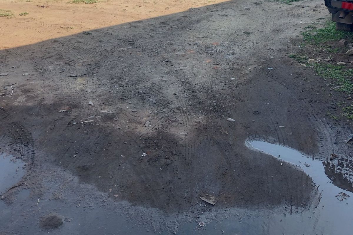 An unpaved, muddy residential plot area showing signs of poor drainage and uneven terrain.