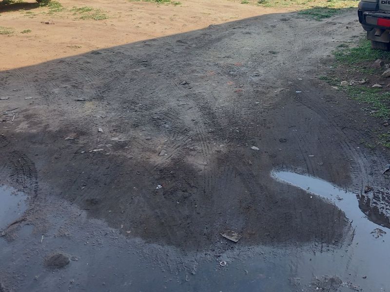 An unpaved, muddy residential plot area showing signs of poor drainage and uneven terrain.