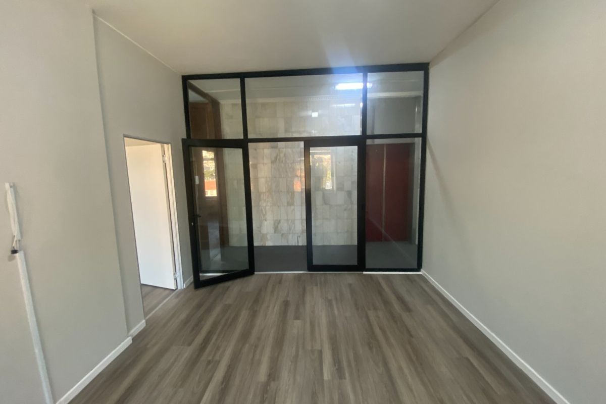 A bright, empty office space featuring modern laminate flooring and a sleek black aluminium-framed glass partition wall.