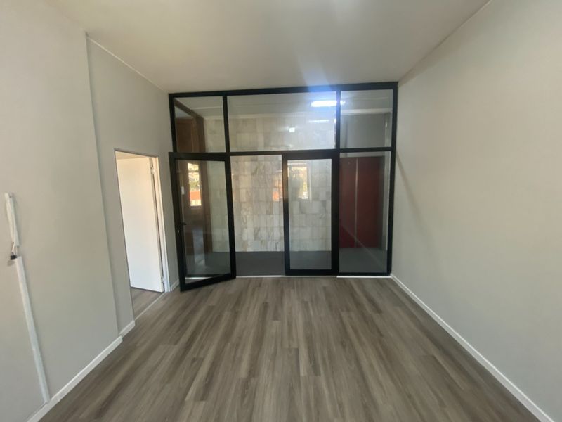 A bright, empty office space featuring modern laminate flooring and a sleek black aluminium-framed glass partition wall.