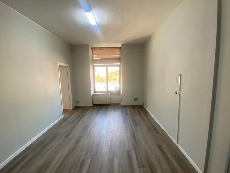 A vacant, well-lit office space featuring modern laminate flooring, a window with blinds, and an integrated HVAC unit.