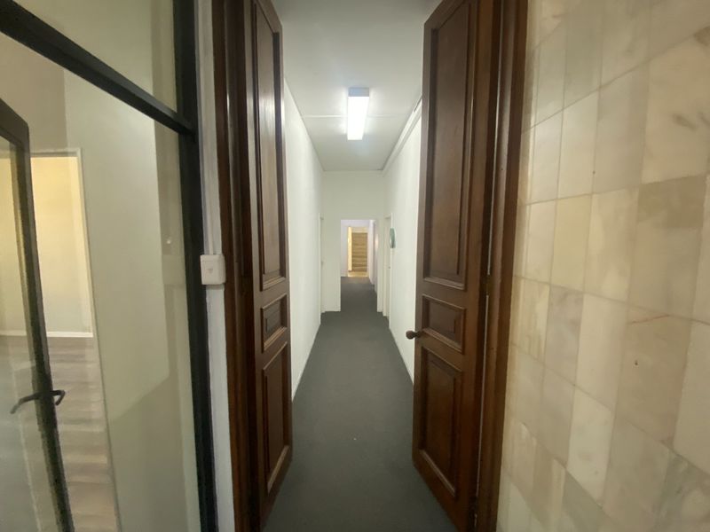 A long commercial hallway featuring double wooden doors, carpeted flooring, and tiled wall accents, leading to an interior office space.