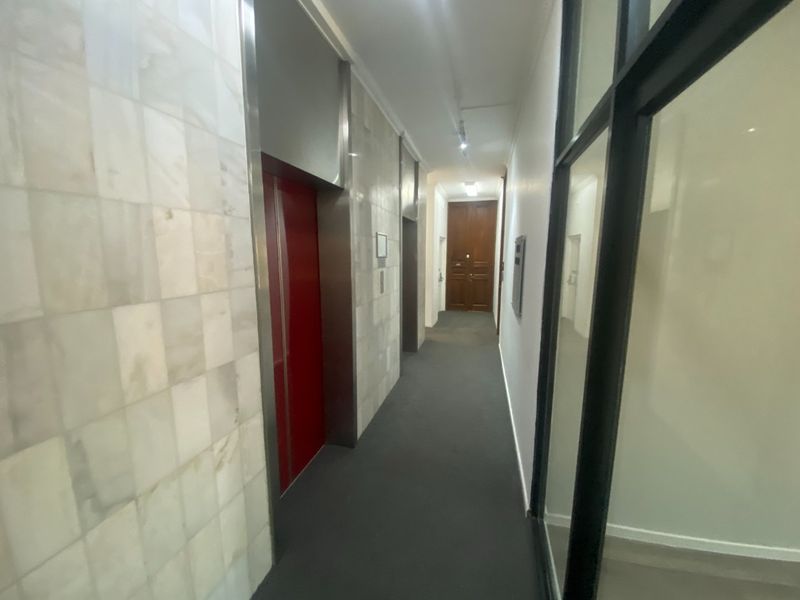 A commercial hallway featuring marble wall cladding, an elevator access point, and a glass partition wall with neutral carpeting.