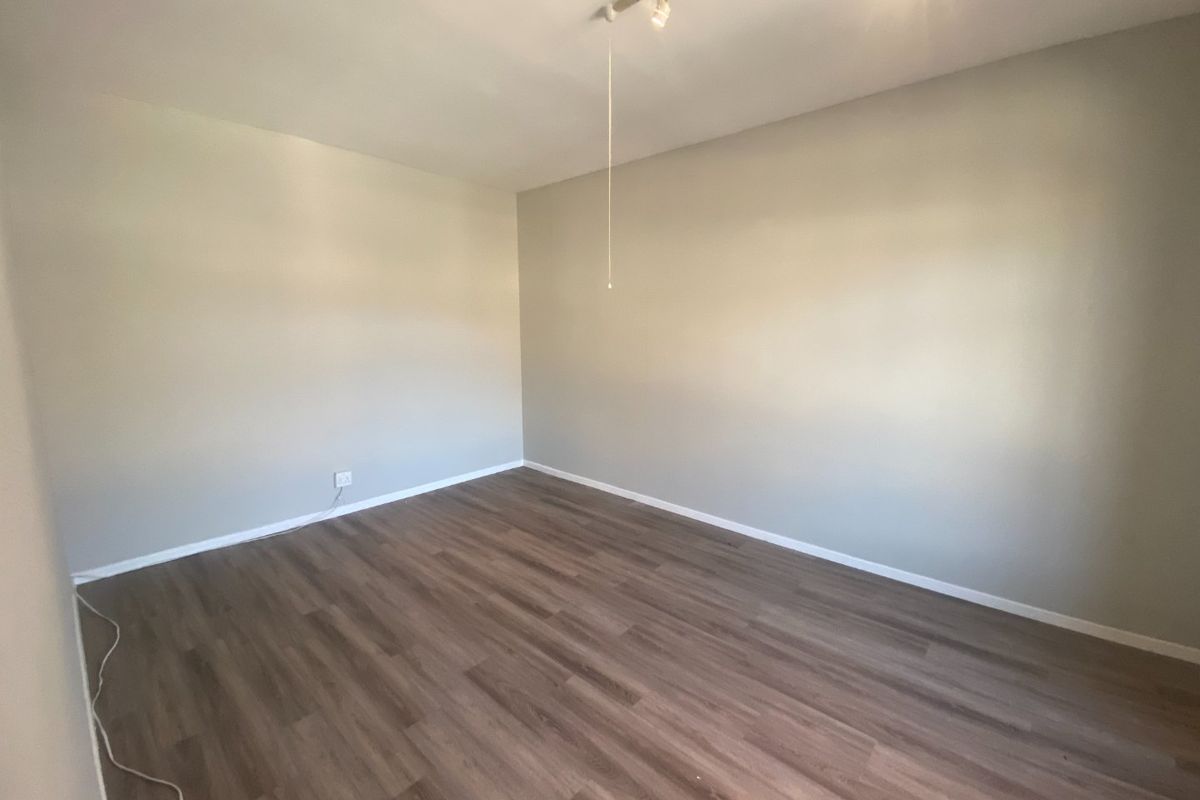 A clean, empty bedroom featuring modern laminate wood-look flooring and track lighting, providing a neutral canvas for various commercial or residential uses.