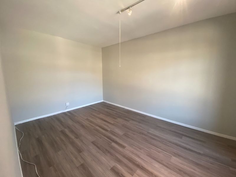 A clean, empty bedroom featuring modern laminate wood-look flooring and track lighting, providing a neutral canvas for various commercial or residential uses.