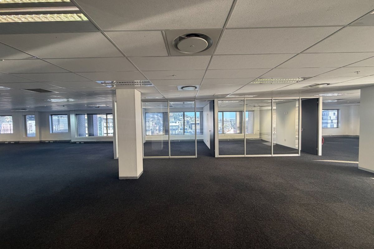 Spacious open-plan commercial office space featuring glass-partitioned meeting rooms, suspended ceilings with recessed lighting, and expansive city views.
