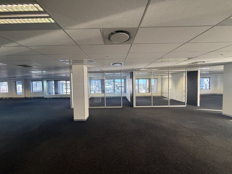 Spacious open-plan commercial office space featuring glass-partitioned meeting rooms, suspended ceilings with recessed lighting, and expansive city views.