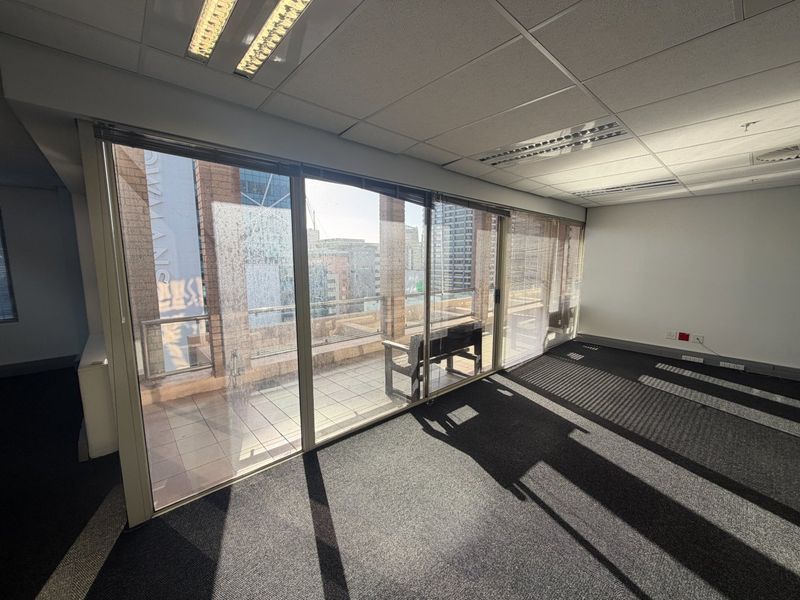 Empty commercial office space featuring carpeted flooring, suspended ceilings with recessed lighting, and large sliding glass doors providing access to an outdoor balcony area.